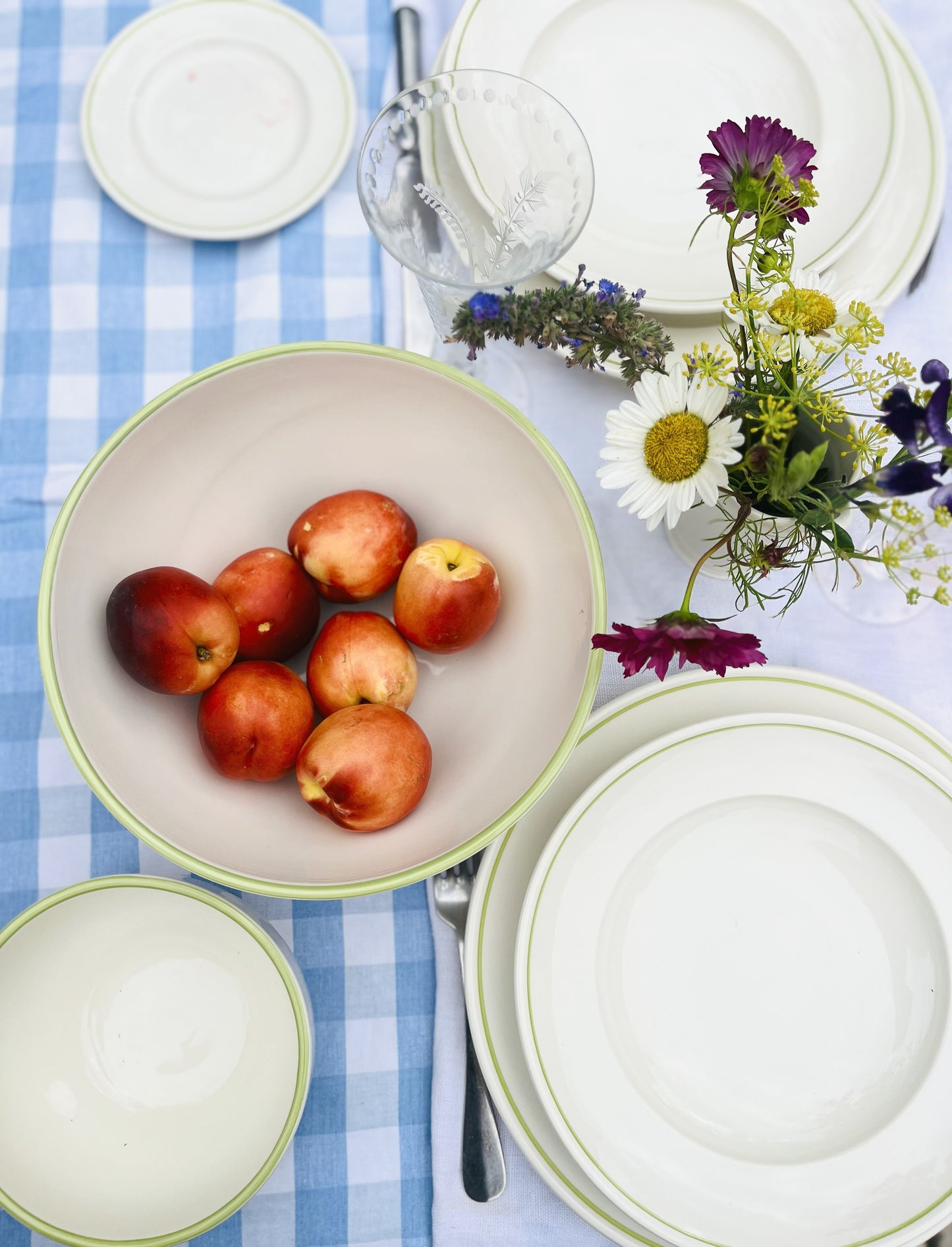 Bowl of peaches on a table with porcelain Clover Green plates, cutlery, and flowers.