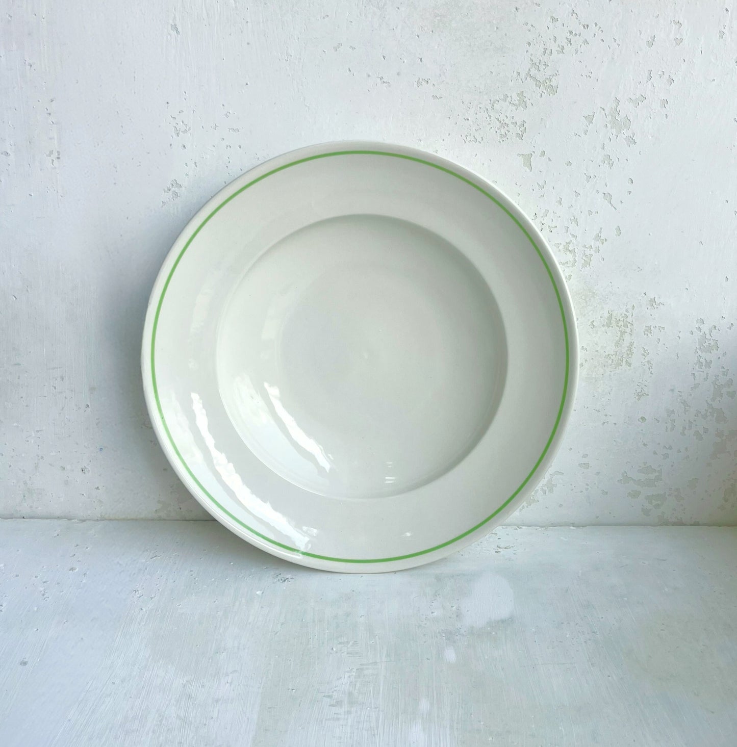 White porcelain pasta bowl with a clover green rim on a textured white background