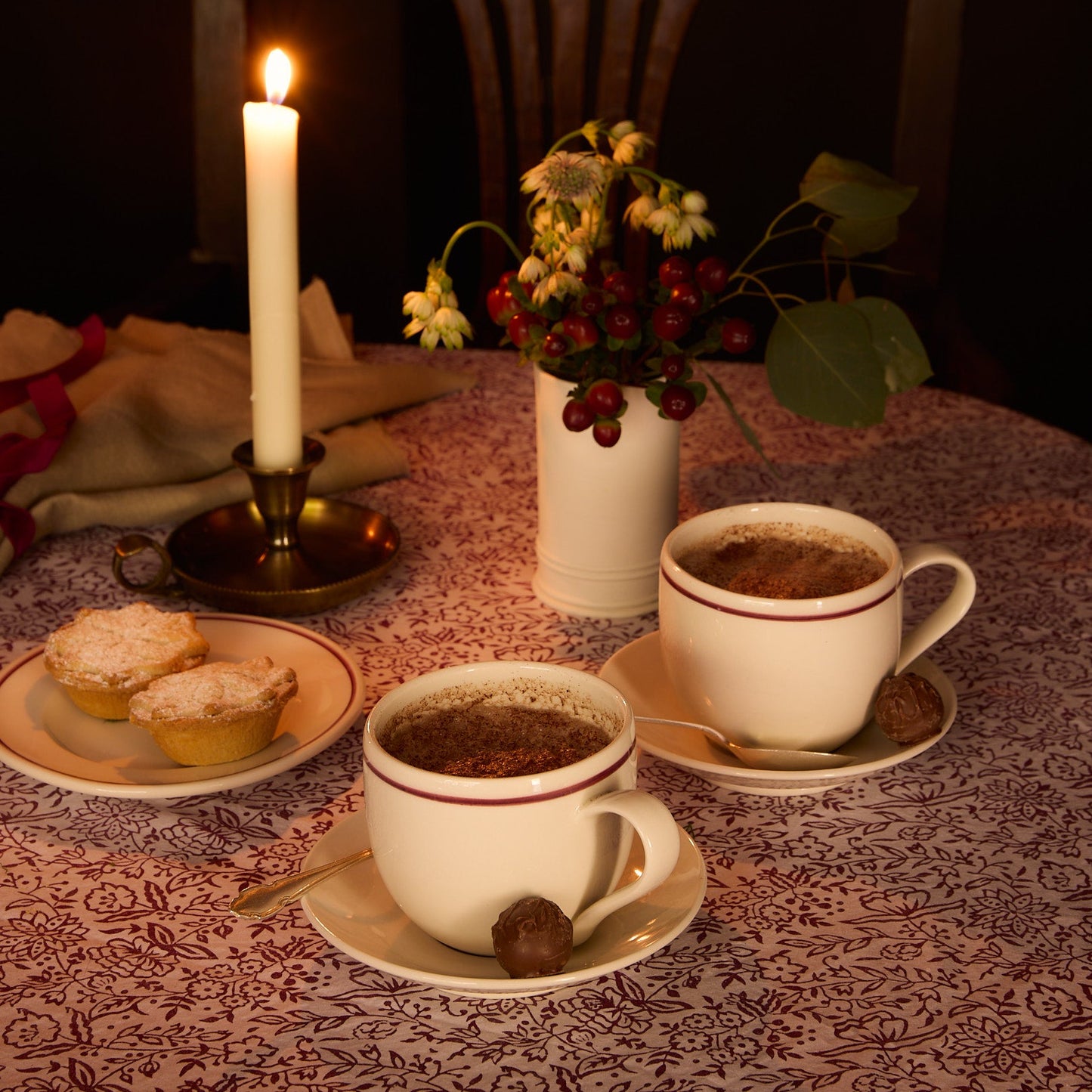 Hot chocolate with mince pies on a patterned tablecloth, candlelit ambiance