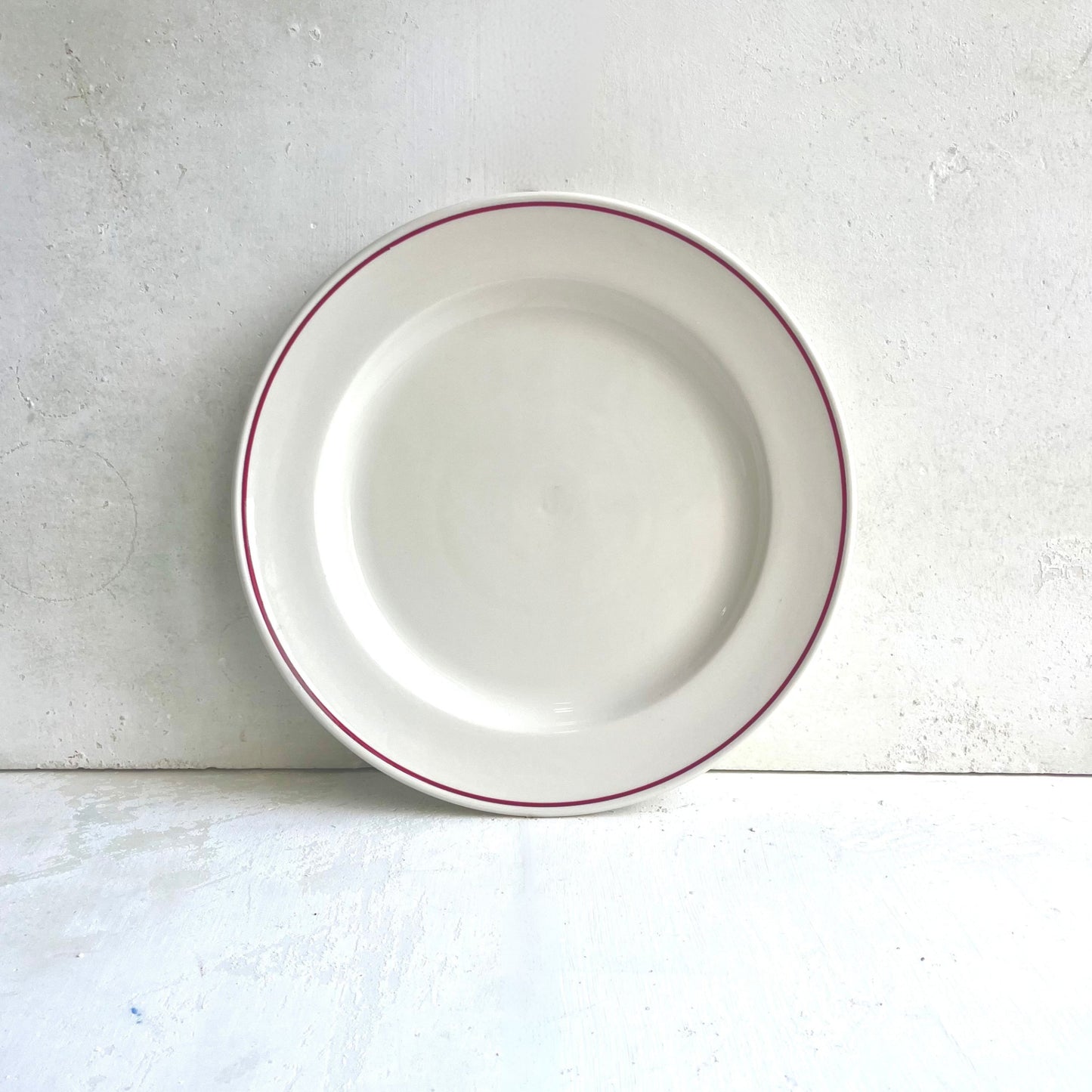 White porcelain ceramic plate with a Burgundy Line on rim on a light gray surface