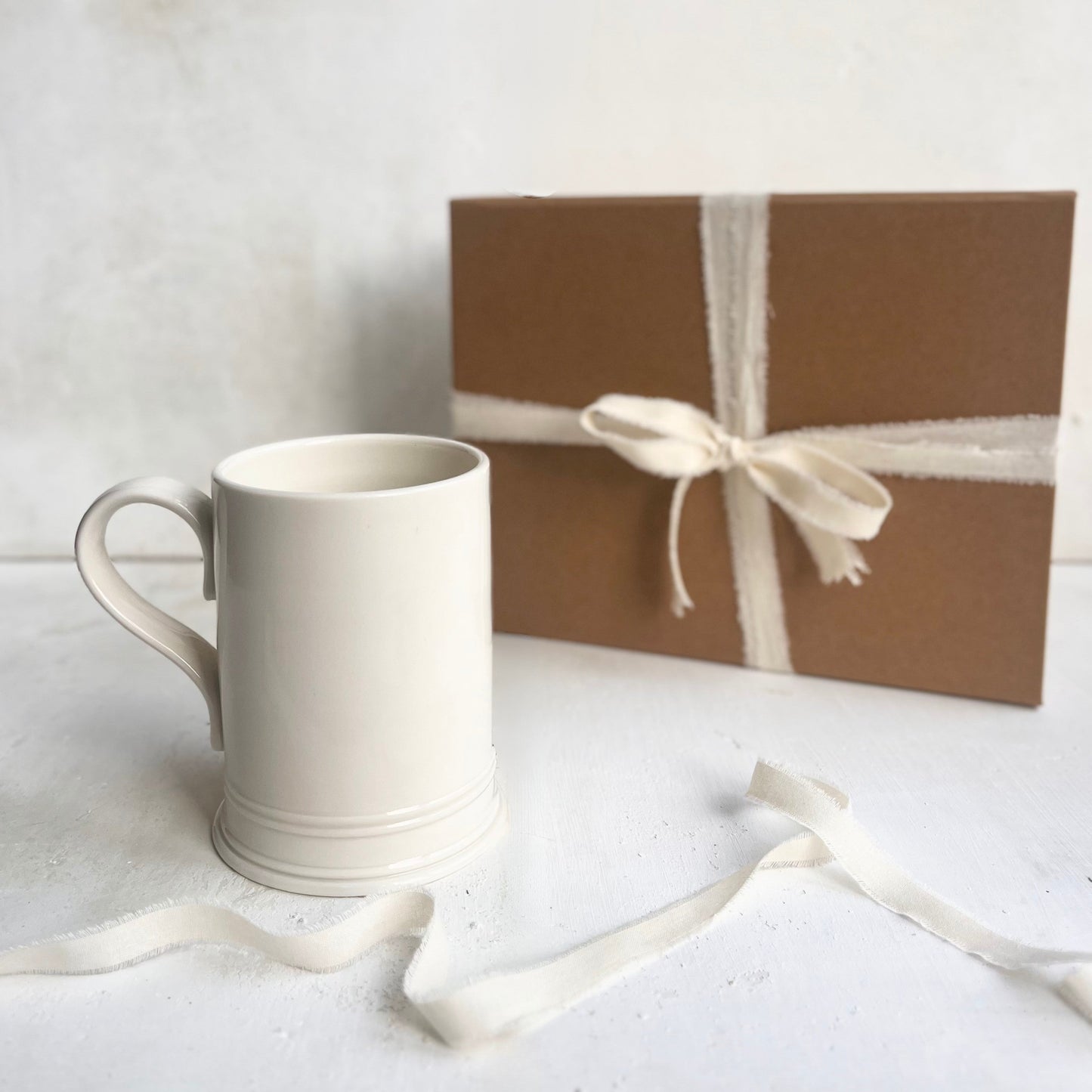 White mug and brown gift box with white ribbon on a light background