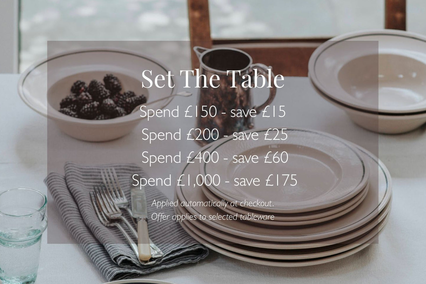 Dining table setting with John Julian Stoneware plates, and cutlery with promotional text overlay - spend £150 and save £15.